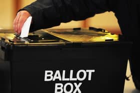 A person posting their voting slip into a black ballot box