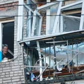 A man looks through a broken window in a residential house bearing a Ukraine flag