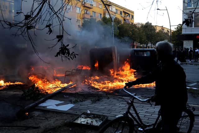 A man passes a burning barricade during clashes in Tirana (Hameraldi Agolli/AP)