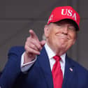 Donald Trump in a red baseball cap points towards a crowd at a rally
