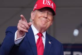 Donald Trump in a red baseball cap points towards a crowd at a rally