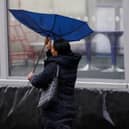 A woman's umbrella blows inside out while she is walking in strong wind
