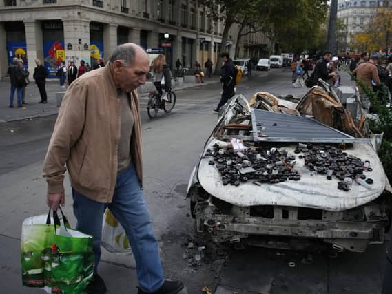 A man walks past a burned-out car in Paris after a quiet Monday night under curfew