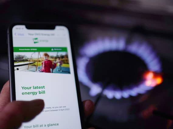 A household energy bill displayed on a mobile phone held next to a gas hob