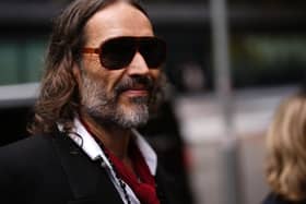 Russell Brand smiling while walking outside court, wearing sunglasses