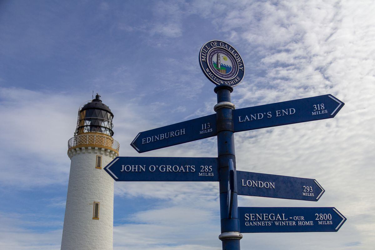 Sign post in front of the Mull of Galloway lighthouse in Dumfries and Galloway, Scotland, United Kingdom under a blue sky with white clouds