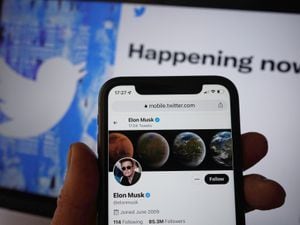 Elon Musk's Twitter account on a smartphone held in front of a screen showing the Twitter bird icon
