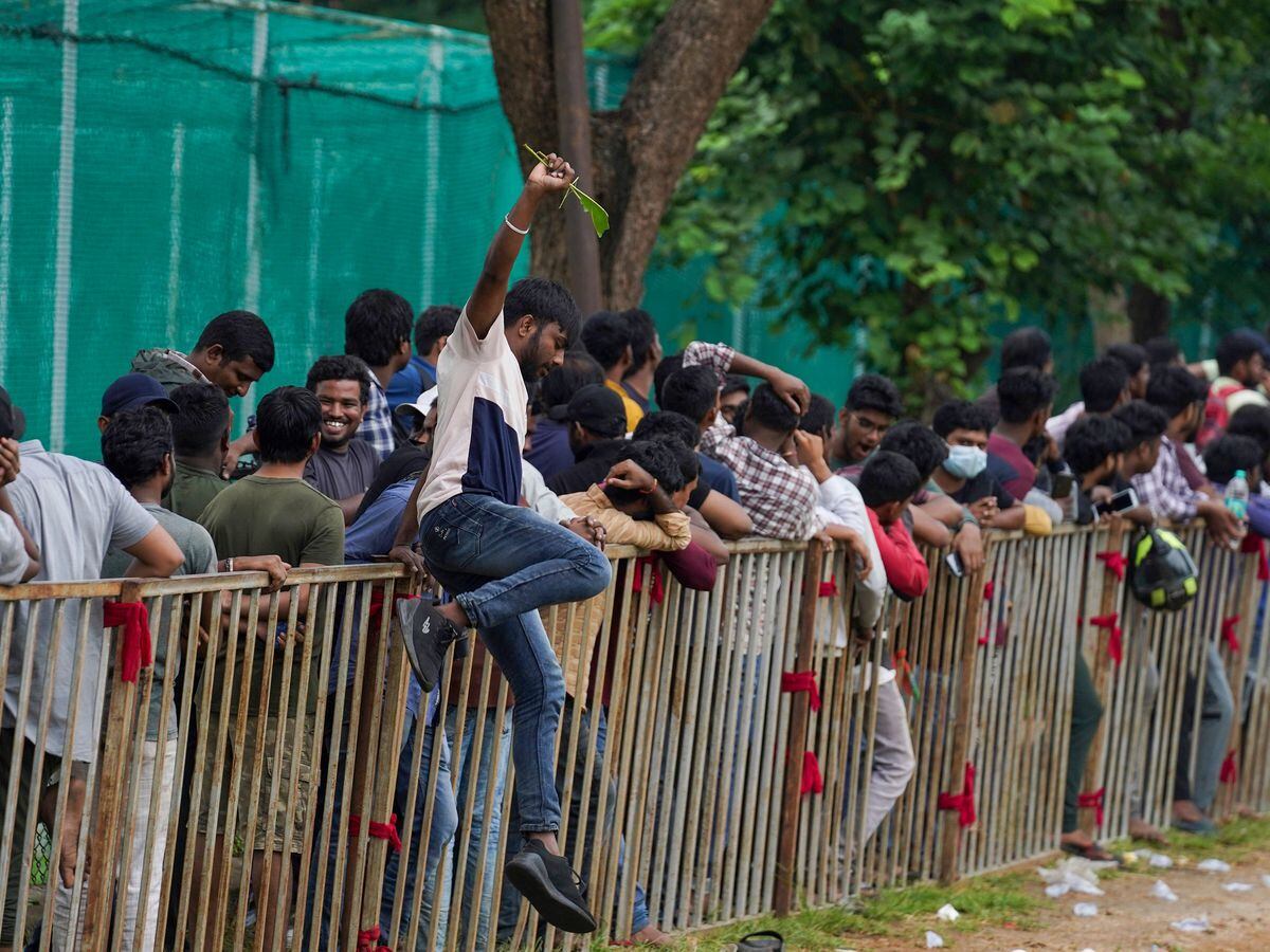A man jumps a railing to take a break as people line up to buy tickets for the third Twenty20 cricket match between India and Australia at Gymkhana grounds in Hyderabad, India