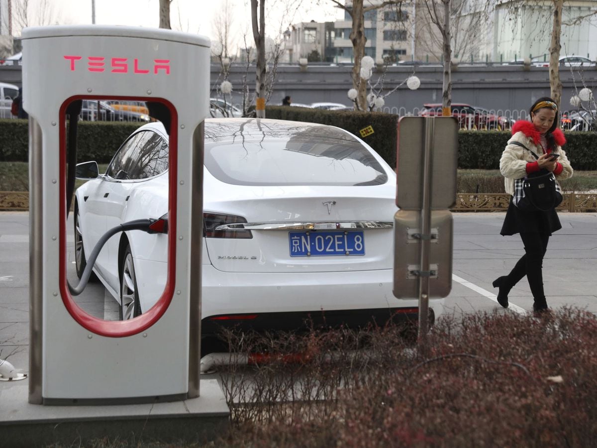 A woman walks past a Tesla car being charged in Beijing