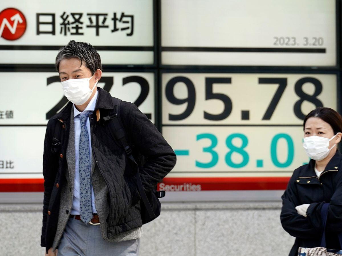 People walk in front of a board showing Japan's Nikkei 225 index