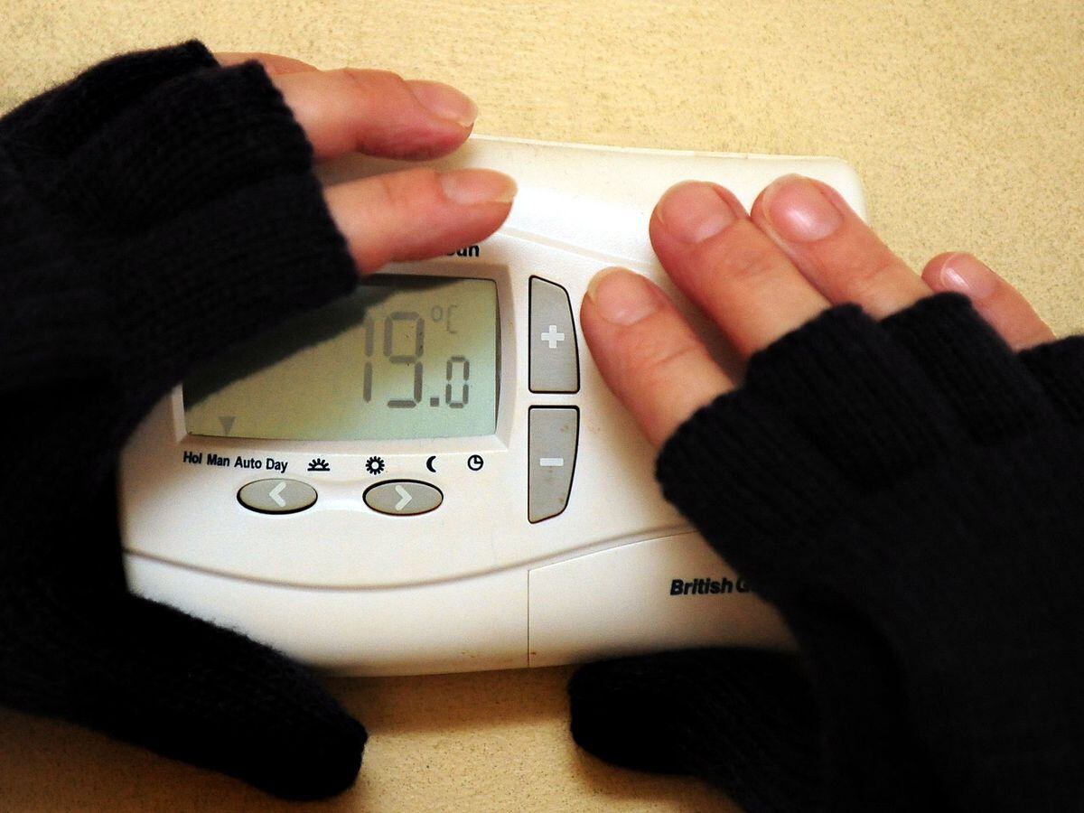 A person wearing gloves adjusts a central heating thermostat
