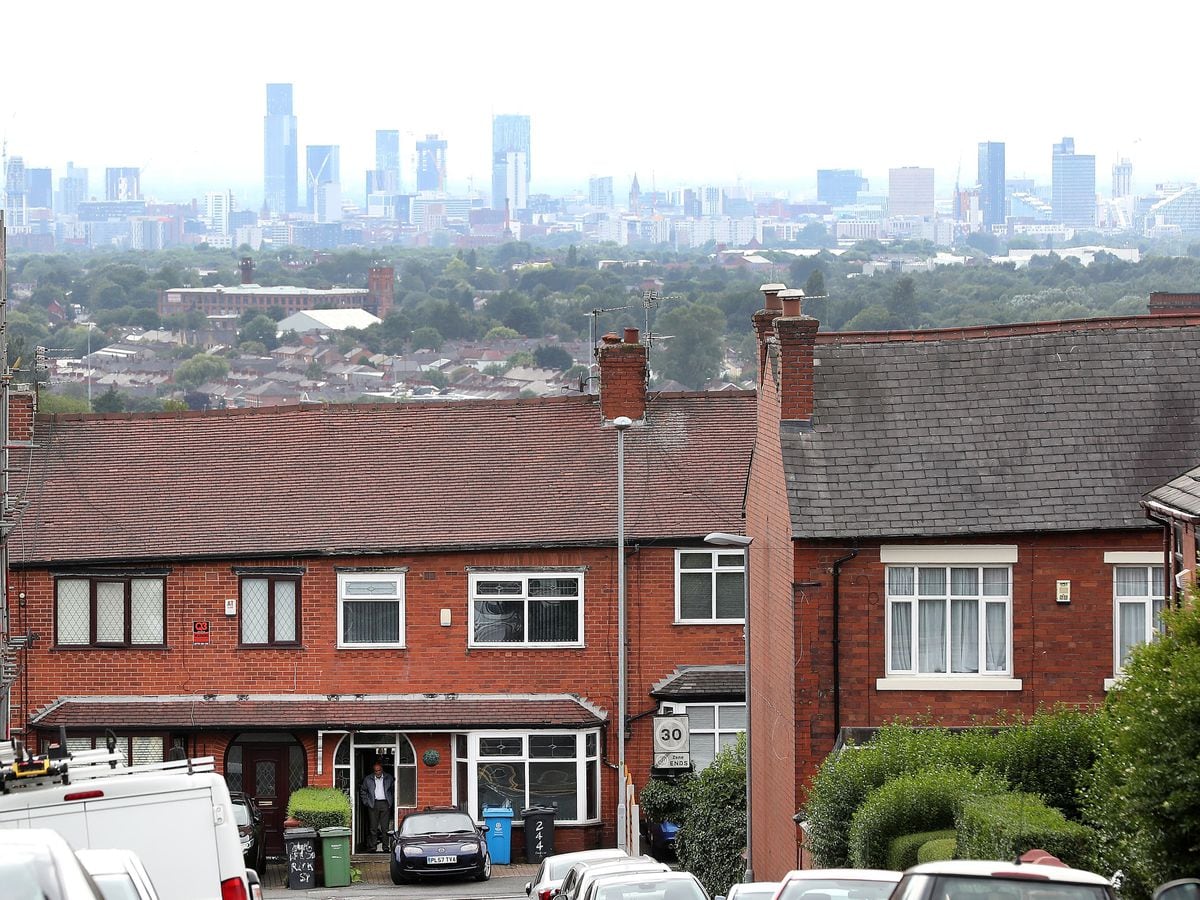 A Resident in Oldham stands in his doorway with the Manchester skyline behind (Martin Rickett/PA)