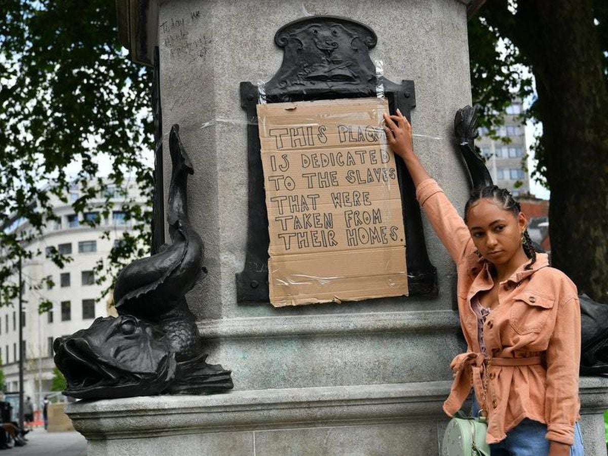 Asha Gwatkin, from Bristol, holds a placard on top of a plinth praising slave trader Edward Colston