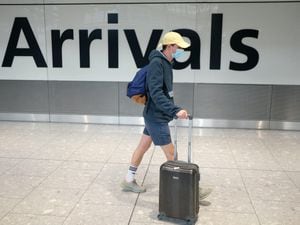 A man wearing a mask walks past an airport arrivals sign