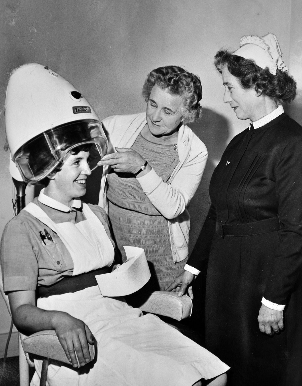 Hair we go... Matron Irene Braithwaite watches as a new hair drier at the Wrekin Hospital is tried out on Nurse Kathleen Davies of Hadley in July 1964. Placing the drier in position is Mrs Marjorie Bebb, chairman of the League of Friends.
