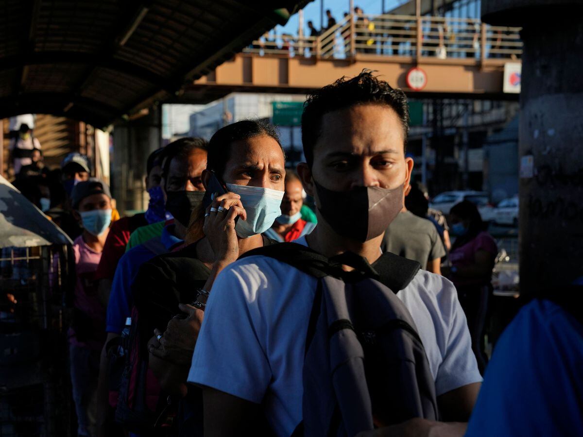 Commuters wearing face masks wait for a ride at a bus stop in Manila, Philippines
