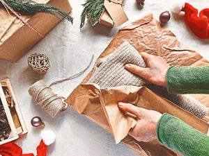 Woman's hands wrapping woolen sweater in craft recycled paper on the table with christmas decoration. Natural aesthetic. Zero waste. Packaging of Christmas gifts.Winter holiday celebration. Top view.
