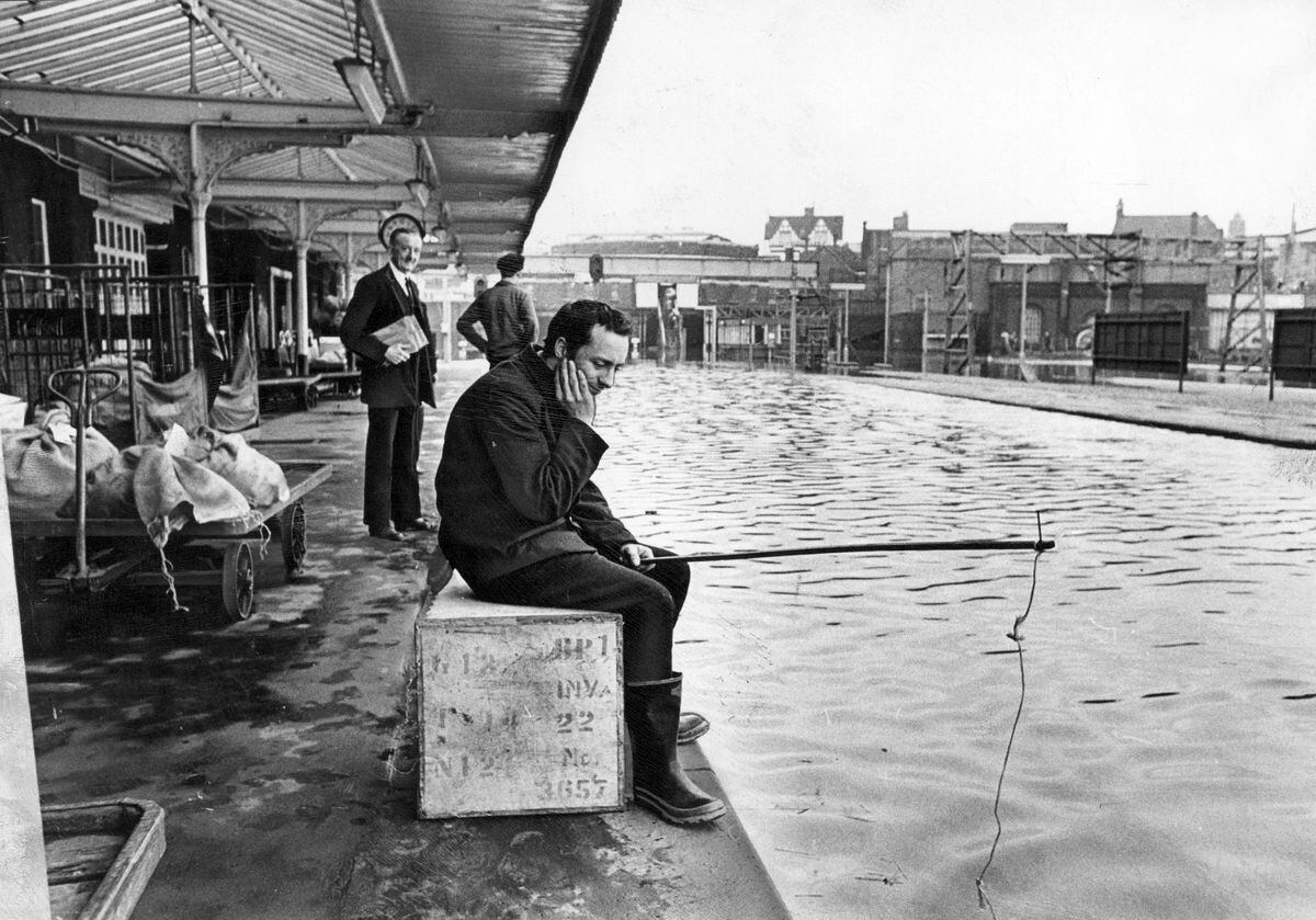 Well, that's one way to try to catch a train. Porter Terry Nightingale tries his luck with a hook and line at Walsall's flooded railway station in May 1969. 