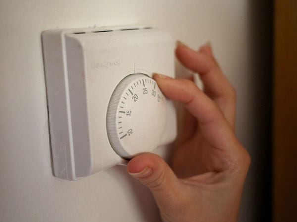 A person adjusts a central heating thermostat