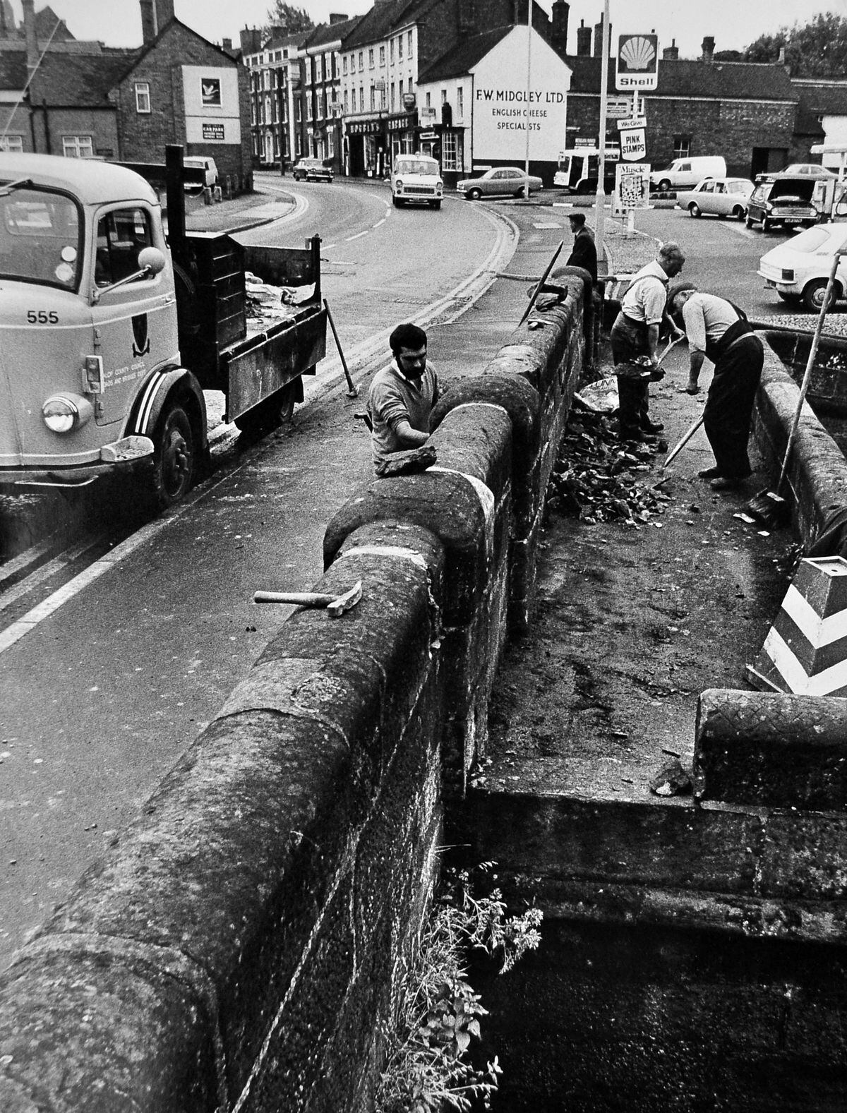 The canal bridge at the bottom of the High Street, an ancient monument, was damaged badly when it was hit by a car in 1974. County council workers were photographed repairing it the following week