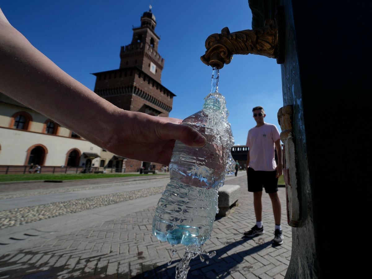 Tourists fill plastic bottles with water from a public fountain at the Sforzesco Castle in Milan, Italy