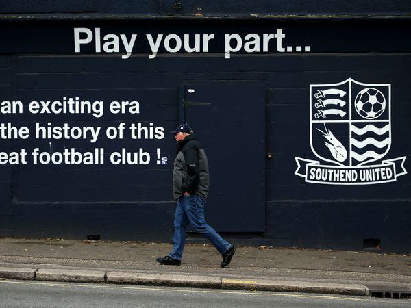 A person walking past a hoarding featuring the Southend United badge