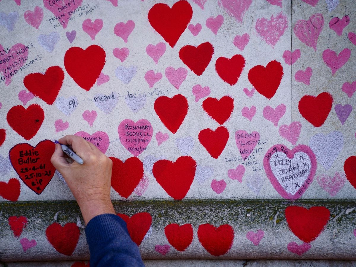 A man writes on a heart at the National Covid Memorial Wall, in Westminster