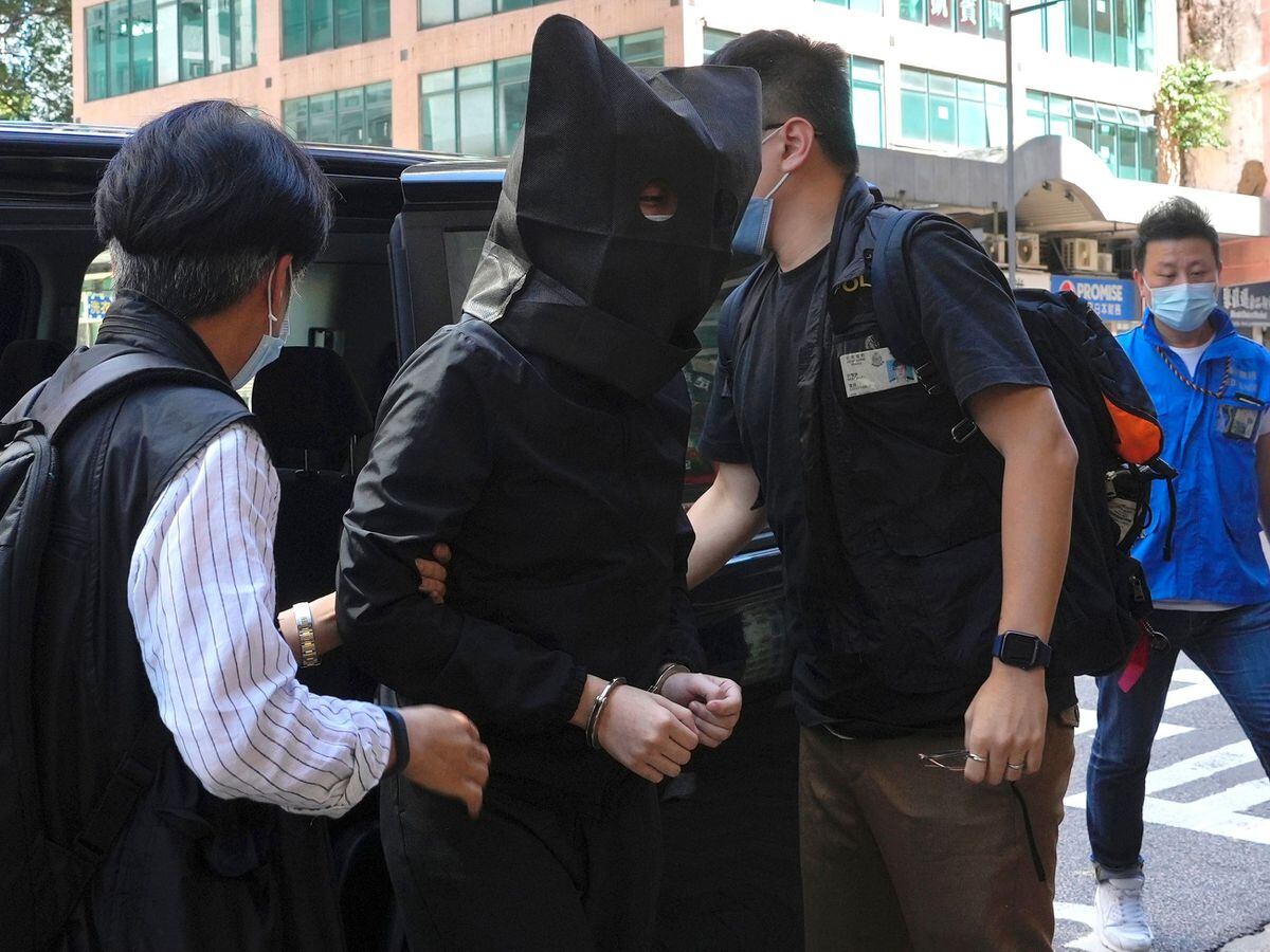 A hooded suspect is accompanied by police officers to searchfor evidence at an office in Hong Kong (Vincent Yu/AP)