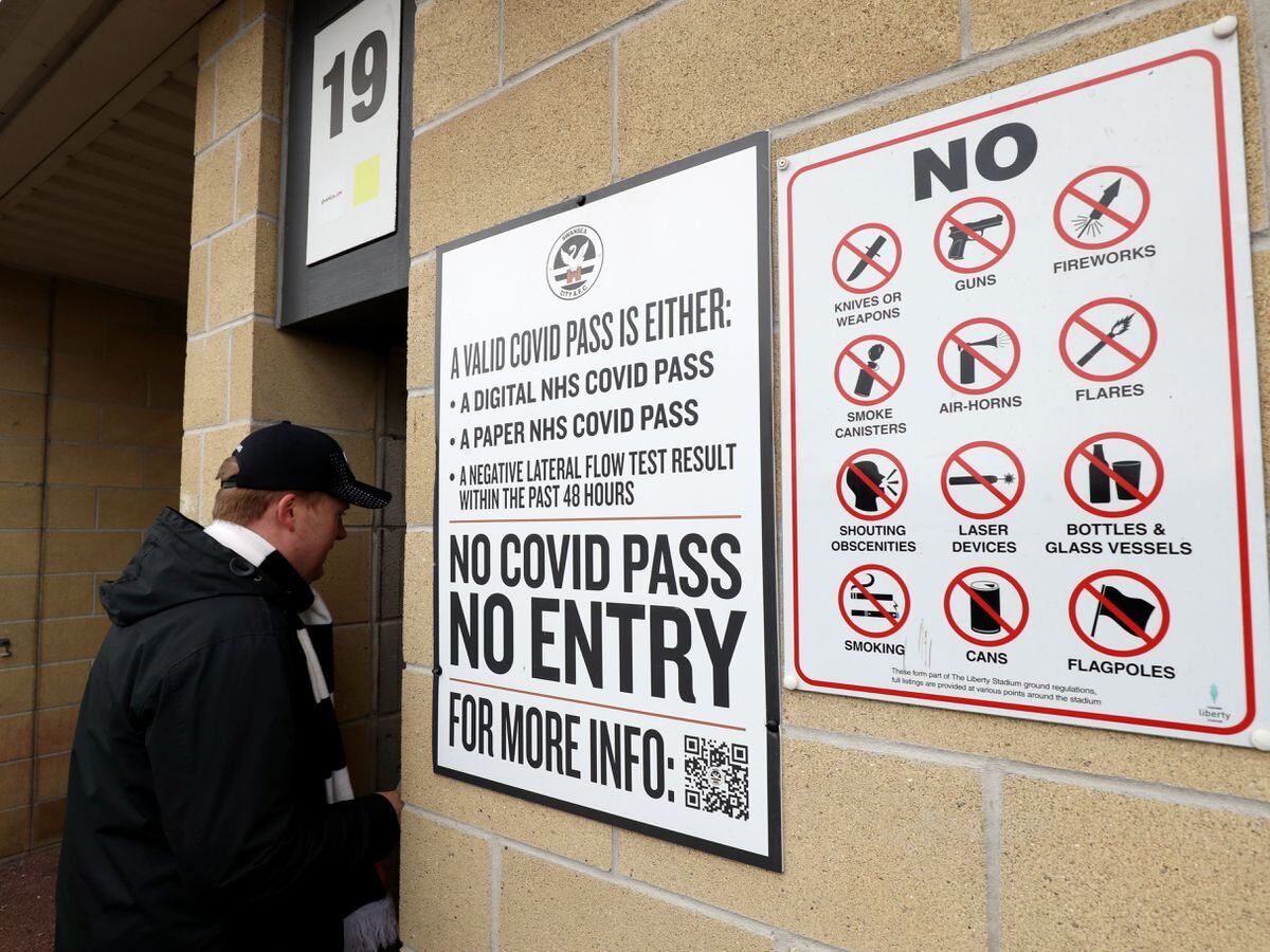 A Swansea City fan enters the team's stadium next to a notice about requirements for a Covid pass (Bradley Collyer/PA)