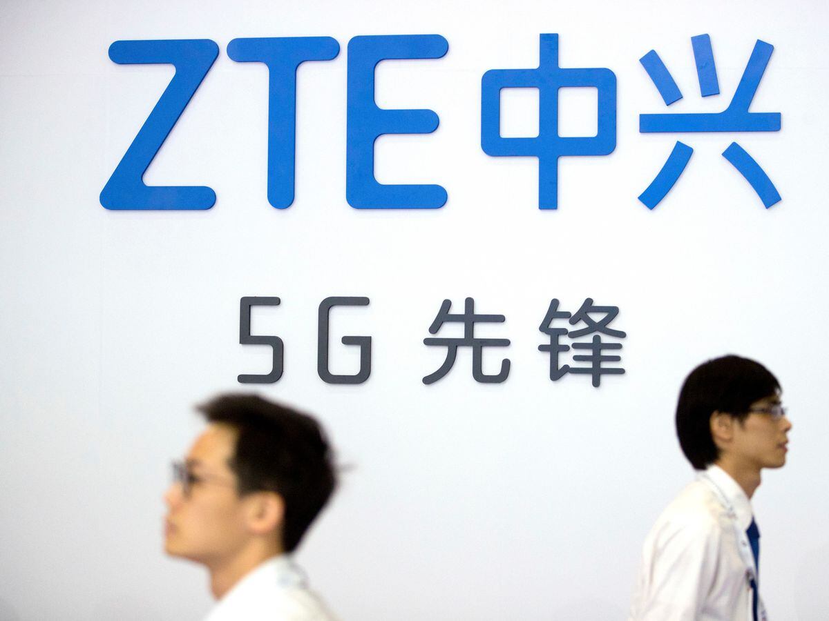 Visitors walk past a display from Chinese technology firm ZTE at the PT Expo in Beijing