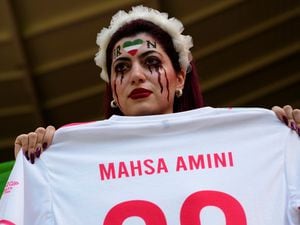 A woman holds a shirt with the name of Mahsa Amini, a woman who died while in police custody in Iran at the age of 22, as she takes her place in the stands ahead of the World Cup group B soccer match between Wales and Iran at the Ahmad Bin Ali Stadium in Al Rayyan, Qatar