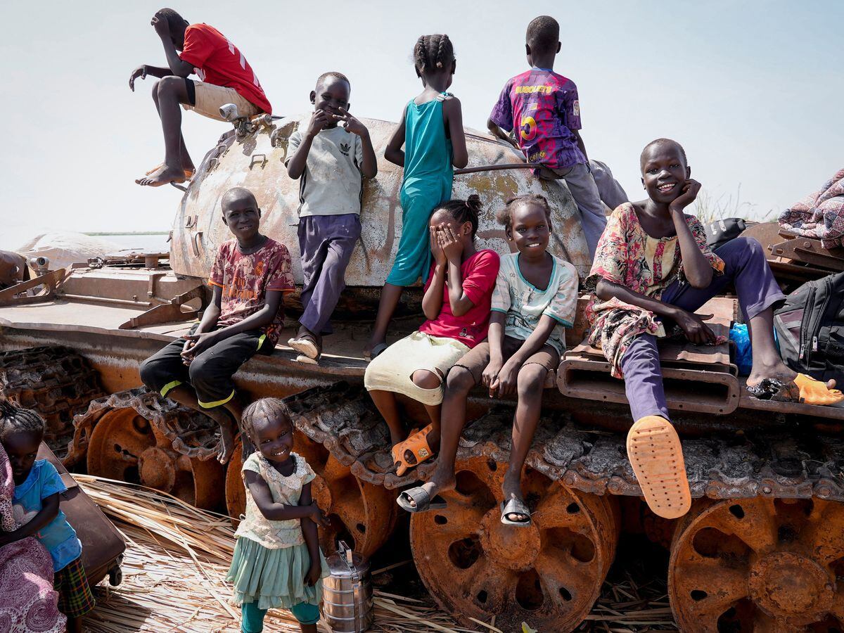 Children sit and play on the remains of a tank at the river port in Renk